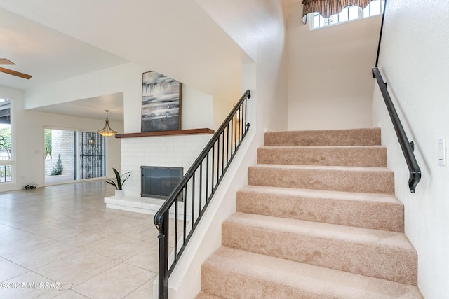 staircase featuring a fireplace, a ceiling fan, and tile patterned floors