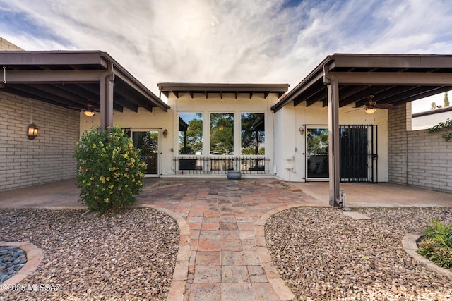 exterior space featuring brick siding, ceiling fan, stucco siding, and a patio