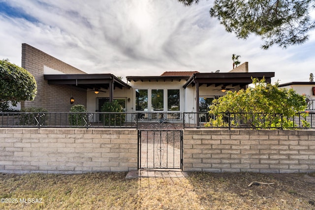 view of front facade featuring ceiling fan, a fenced front yard, a gate, and stucco siding