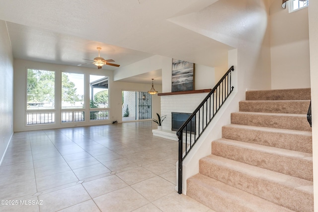 stairway featuring a ceiling fan, tile patterned flooring, a brick fireplace, and baseboards