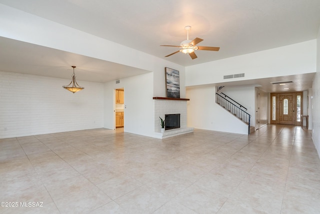 unfurnished living room featuring visible vents, ceiling fan, brick wall, stairs, and a fireplace