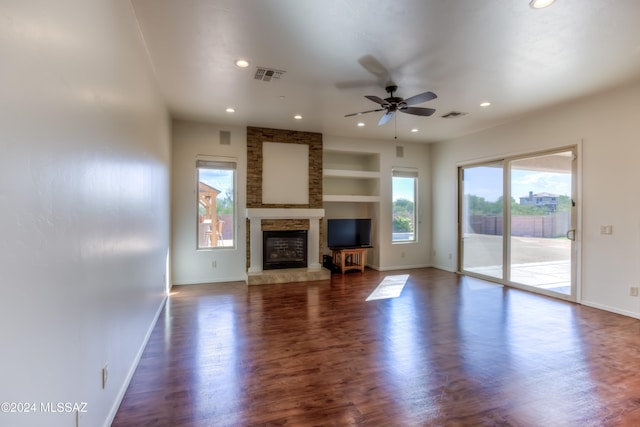 unfurnished living room with ceiling fan, a stone fireplace, dark hardwood / wood-style floors, and built in shelves