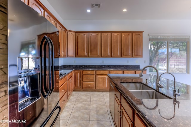 kitchen featuring black fridge with ice dispenser, dark stone countertops, dishwasher, light tile patterned flooring, and sink