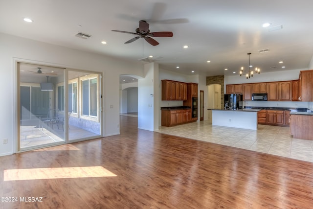 unfurnished living room featuring arched walkways, visible vents, light wood finished floors, and ceiling fan with notable chandelier