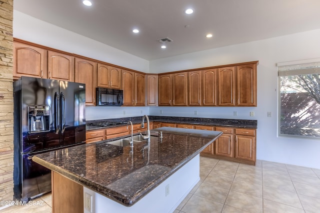 kitchen with dark stone counters, a center island with sink, sink, black appliances, and light tile patterned floors