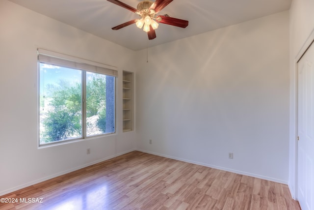 spare room featuring light wood-type flooring, a ceiling fan, built in features, and a healthy amount of sunlight