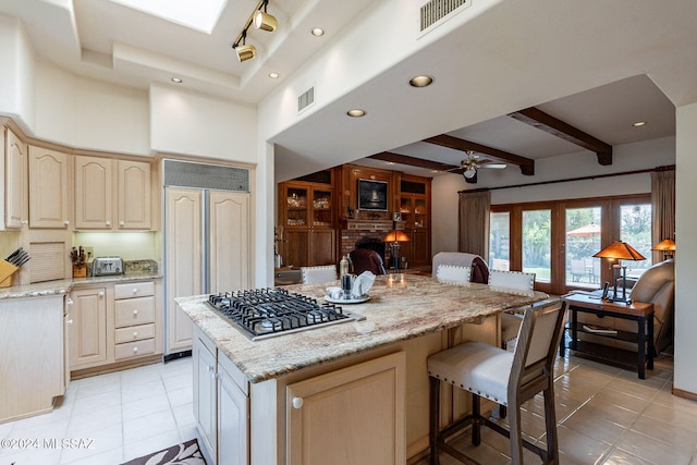 kitchen with light stone countertops, ceiling fan, a center island, paneled built in fridge, and stainless steel gas cooktop