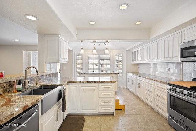 kitchen featuring white cabinets, hanging light fixtures, light stone counters, kitchen peninsula, and stainless steel appliances