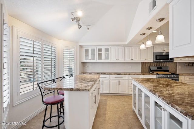 kitchen featuring white cabinetry, appliances with stainless steel finishes, a center island, and dark stone counters