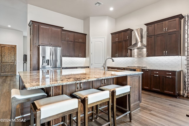 kitchen featuring a center island with sink, a kitchen breakfast bar, sink, wall chimney exhaust hood, and stainless steel appliances