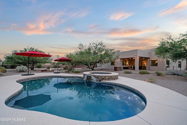 pool at dusk featuring a patio area and an in ground hot tub