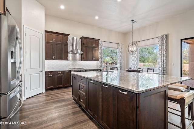 kitchen with light stone countertops, stainless steel fridge, a center island with sink, and pendant lighting