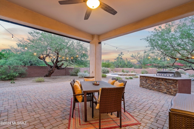 patio terrace at dusk featuring a grill, ceiling fan, and exterior kitchen