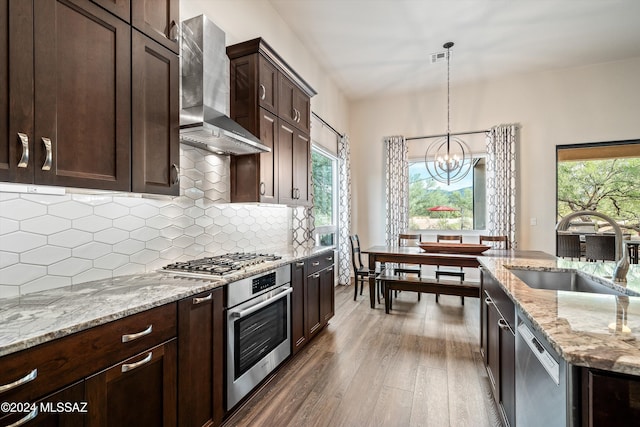 kitchen featuring sink, hanging light fixtures, wall chimney exhaust hood, appliances with stainless steel finishes, and tasteful backsplash