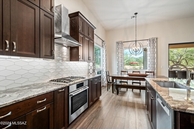 kitchen featuring sink, appliances with stainless steel finishes, hanging light fixtures, backsplash, and wall chimney exhaust hood