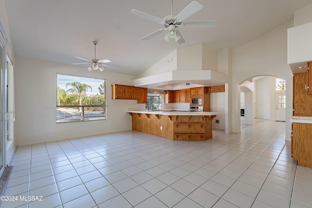 kitchen featuring ceiling fan, stainless steel microwave, high vaulted ceiling, kitchen peninsula, and light tile patterned flooring