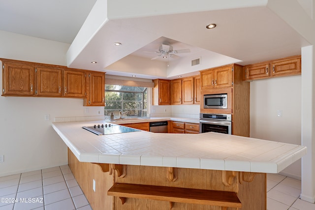 kitchen featuring sink, ceiling fan, tile counters, kitchen peninsula, and stainless steel appliances