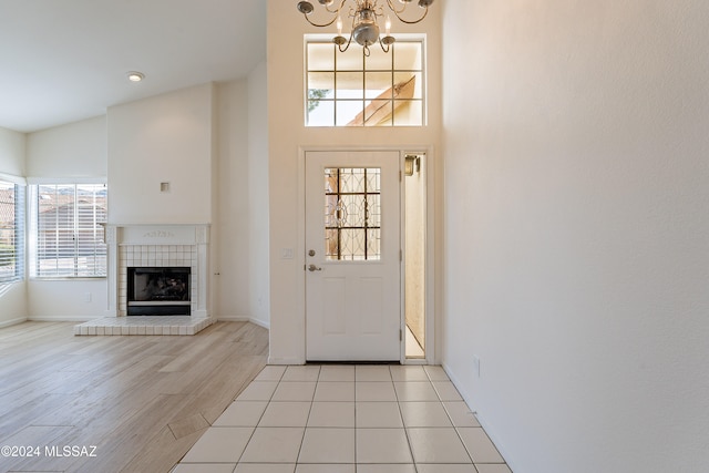 entryway with a chandelier, high vaulted ceiling, light hardwood / wood-style flooring, and a tile fireplace