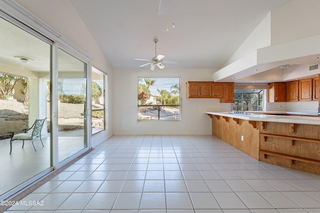 kitchen featuring ceiling fan, high vaulted ceiling, kitchen peninsula, a breakfast bar, and light tile patterned floors