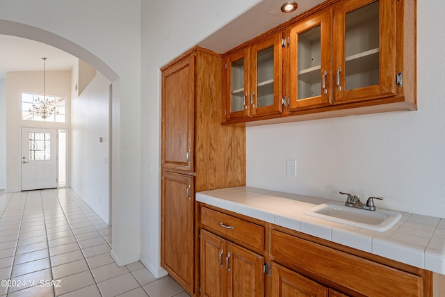 kitchen featuring vaulted ceiling, sink, decorative light fixtures, a chandelier, and tile counters