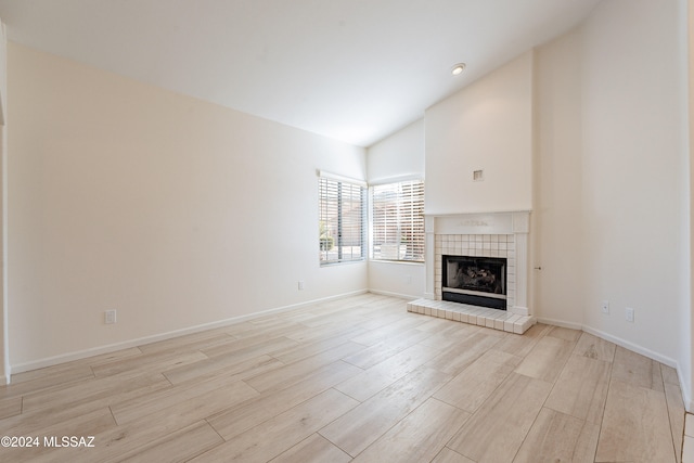 unfurnished living room featuring high vaulted ceiling, light hardwood / wood-style floors, and a tile fireplace