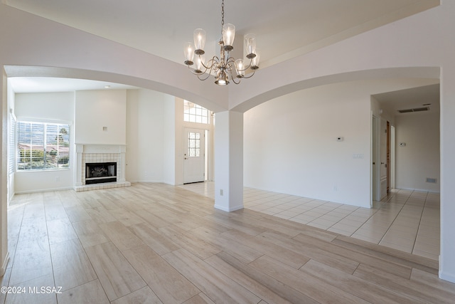 unfurnished living room featuring a tile fireplace, vaulted ceiling, light hardwood / wood-style flooring, and a notable chandelier