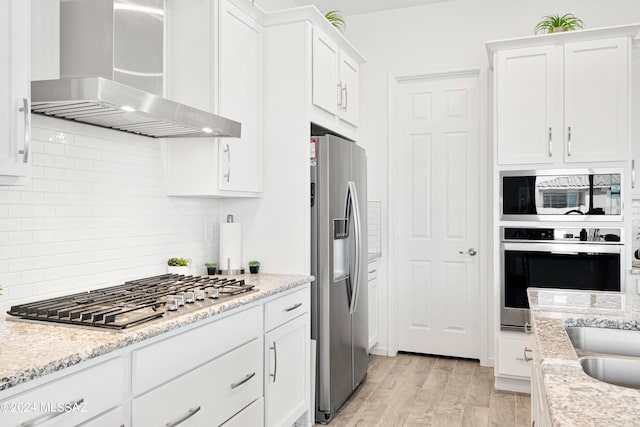 kitchen with wall chimney exhaust hood, white cabinets, stainless steel appliances, and light hardwood / wood-style flooring