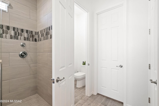 bathroom featuring wood-type flooring, toilet, and tiled shower