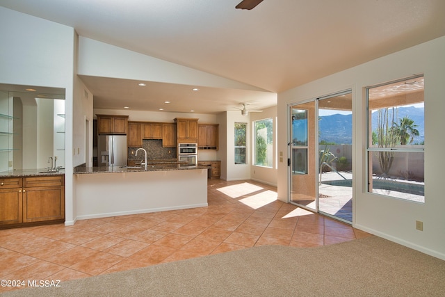 kitchen featuring ceiling fan, brown cabinets, a sink, vaulted ceiling, and stainless steel appliances