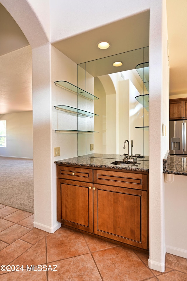 bar featuring light tile patterned floors, stone counters, stainless steel fridge with ice dispenser, and sink