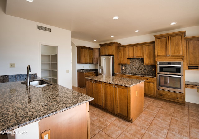 kitchen featuring appliances with stainless steel finishes, dark stone countertops, light tile patterned flooring, and sink