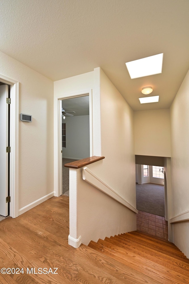stairs with baseboards, wood finished floors, and a skylight
