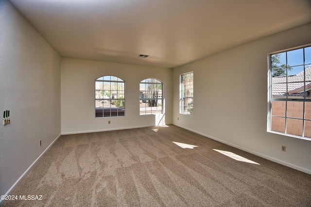 empty room with carpet flooring, baseboards, visible vents, and a healthy amount of sunlight