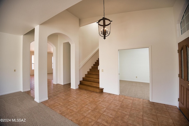 entrance foyer featuring arched walkways, a chandelier, carpet, a towering ceiling, and stairway