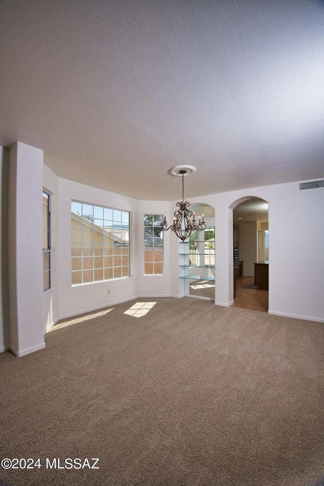 unfurnished room with an inviting chandelier, arched walkways, a textured ceiling, carpet, and visible vents