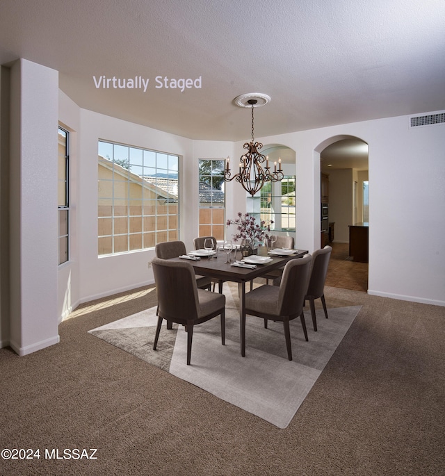 dining space featuring dark colored carpet, a textured ceiling, and a chandelier