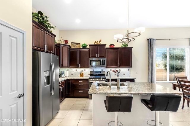 kitchen featuring light stone countertops, decorative backsplash, stainless steel appliances, a center island with sink, and decorative light fixtures