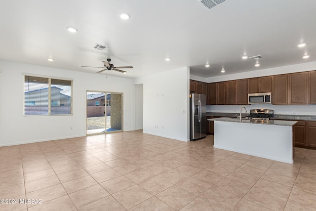 kitchen with ceiling fan, dark stone countertops, a center island with sink, sink, and stainless steel appliances