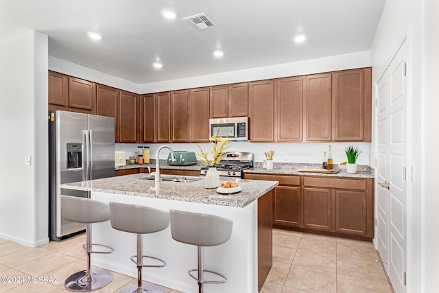 kitchen featuring sink, a center island with sink, stainless steel appliances, a kitchen breakfast bar, and light stone countertops