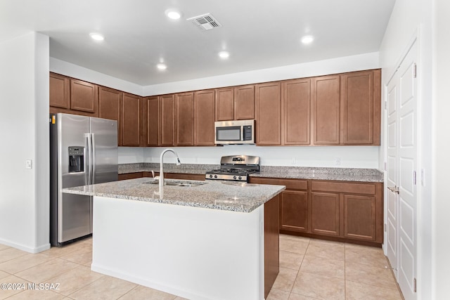 kitchen featuring a center island with sink, light stone counters, sink, and stainless steel appliances