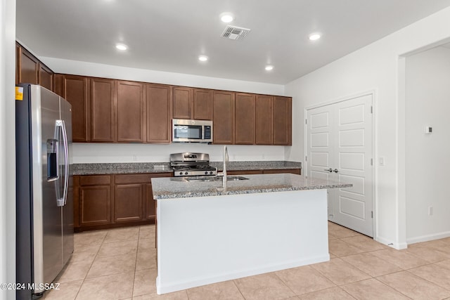 kitchen featuring light stone counters, a kitchen island with sink, sink, appliances with stainless steel finishes, and light tile patterned floors