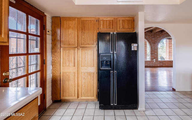 kitchen featuring arched walkways, brick wall, light countertops, light tile patterned floors, and black refrigerator with ice dispenser