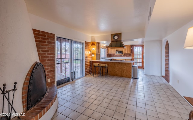 kitchen featuring a kitchen bar, stainless steel microwave, tasteful backsplash, a peninsula, and light tile patterned floors