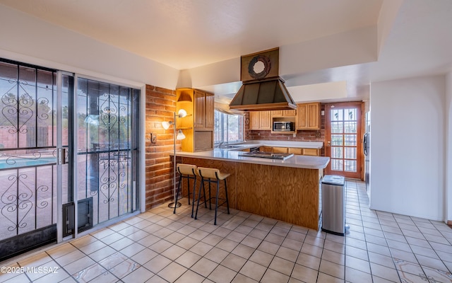 kitchen featuring light tile patterned floors, a peninsula, built in microwave, a sink, and tasteful backsplash