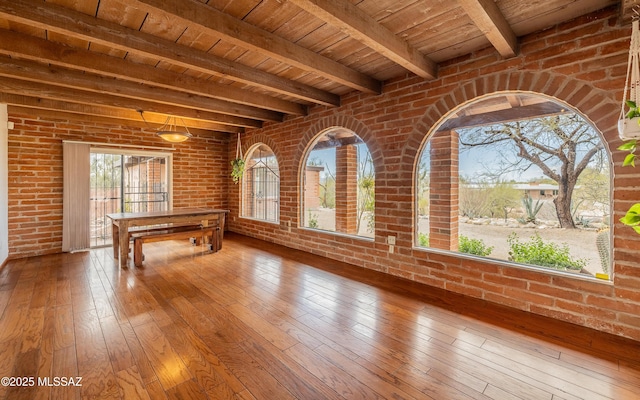 recreation room featuring a wealth of natural light, beam ceiling, brick wall, and wooden ceiling