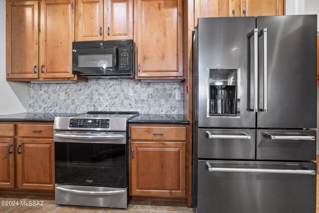 kitchen with brown cabinets, stainless steel appliances, dark countertops, and decorative backsplash