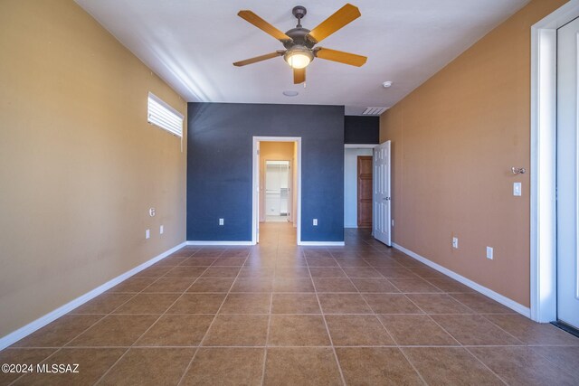 unfurnished bedroom with baseboards, a walk in closet, dark tile patterned flooring, and ceiling fan