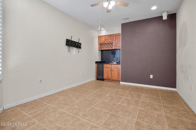 unfurnished living room featuring a sink, wine cooler, baseboards, a ceiling fan, and wet bar
