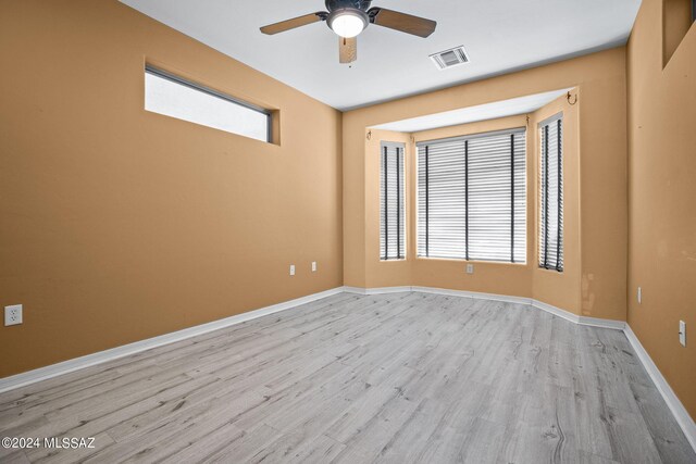 empty room featuring a ceiling fan, visible vents, a wealth of natural light, and light wood-style flooring