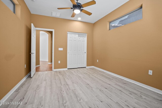 unfurnished bedroom with a closet, visible vents, baseboards, arched walkways, and light wood-style flooring
